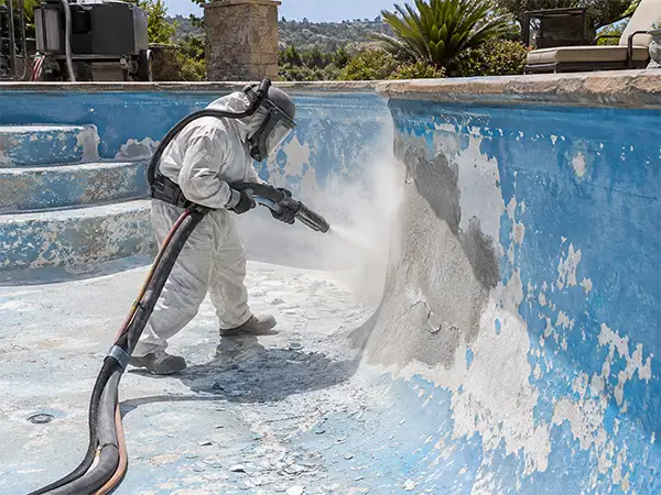 Technician using dustless blasting equipment to remove old coating from an empty swimming pool